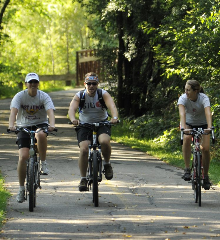 Three adults biking on path surrounded by trees